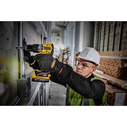 A PERSON USING A DEWALT DCD805 18V XR HAMMER DRILL DRIVER WITH A COMPACT POWERSTACK BATTERY DRILLING A FASTENING HOLE FOR AN ELECTRCAL CLIP