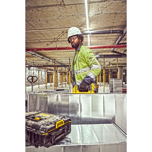 Construction worker using a Grabo 18V XR Suction Lifter to carry metal duct framework, case in foreground