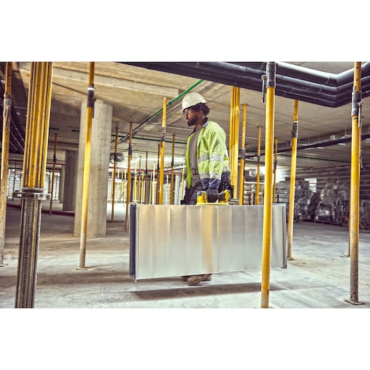 Construction worker using a Grabo 18V XR Suction Lifter to carry metal duct framework in factory