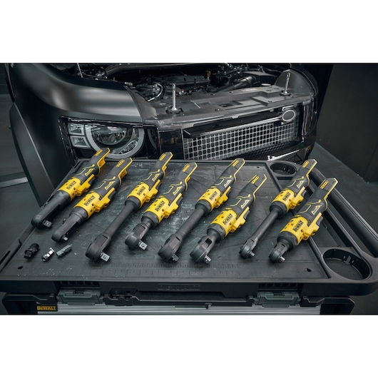 The DEWALT range of 18V XR Brushless Ratchets sitting on top of work unit in front of a car in garage setting.