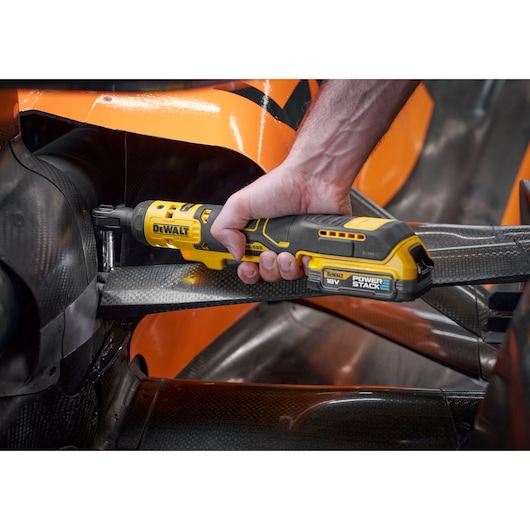 Mechanic using the DEWALT 18V XR Brushless ¼” Ratchet with 18V POWERSTACK battery to tighten bolts on the suspension of the F1 McLaren racing car