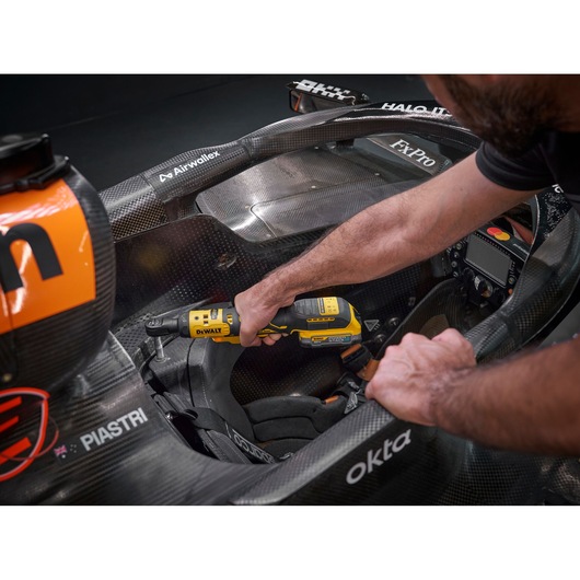 Mechanic using the DEWALT 18V XR Brushless ¼” Ratchet with 18V POWERSTACK battery to tighten bolts in the seat frame cockpit of the F1 McLaren racing car