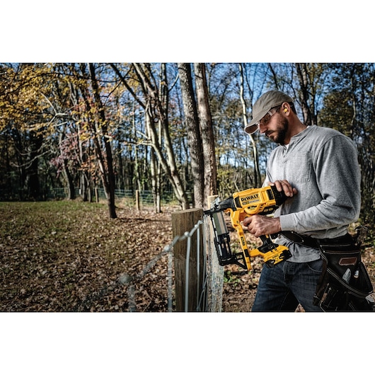 CORDLESS FENCING STAPLER being used on a wooden post by a person