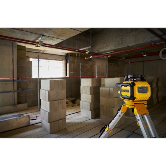 DEWALT Alkaline Rotary Red Beam Laser on tripod on worksite, transmitting horizontal beam over breeze blocks.