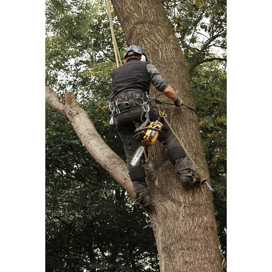 Arborist climbing a tree with the DEWALT 54V XR FLEXVOLT Compact Top Handle Chainsaw attached for use