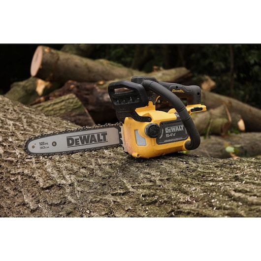 A DEWALT 54V XR FLEXVOLT Compact Top Handle Chainsaw sits on top of a tree trunk