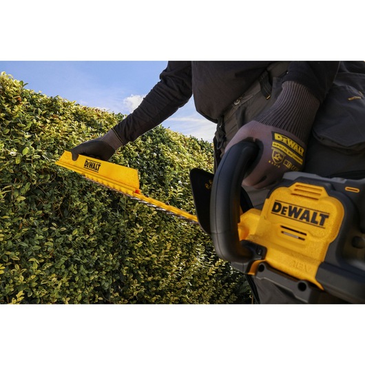 Worker attaching the DEWALT hedge sweep attachment to the DEWALT 18V XR Brushless Hedge Trimmer
