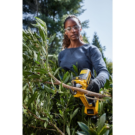 Female user trimming heavy brush using powered cordless pruner Female user trimming heavy brush using powered cordless pruner