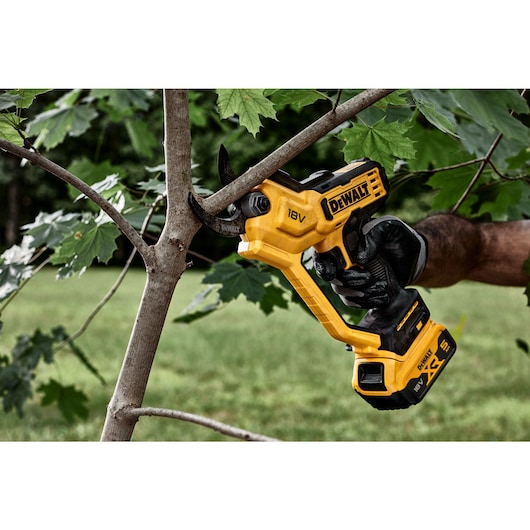 User trimming thick branch using powered cordless pruner