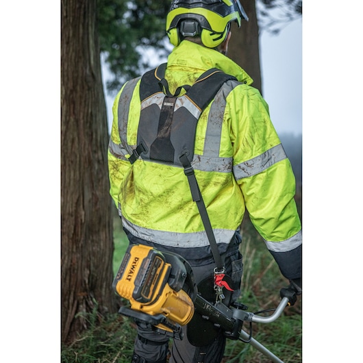Worker wearing the deluxe harness easing the load of the DEWALT 54V String Trimmer (Bull Handle) as walking through forest.