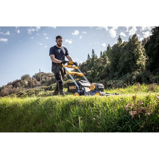 The DEWALT 54V 53cm Self-Propelled Mower being used by landscaper for maintenance in large area, landscaper wearing safety goggles and gloves.