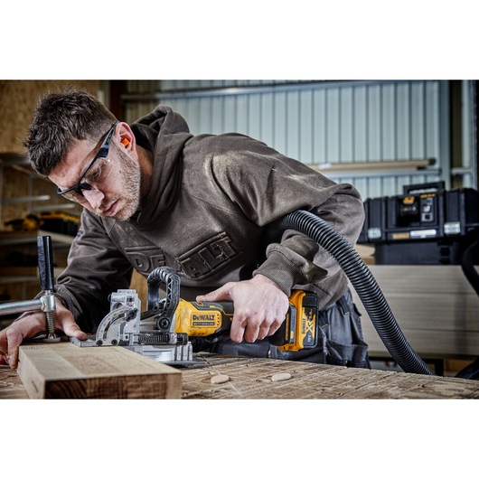 A PERSON USING A DCW682 18V XR BISCUIT JOINTER WITH A 5AH BATTERY ON OAK TIMBER IN A WORKSHOP