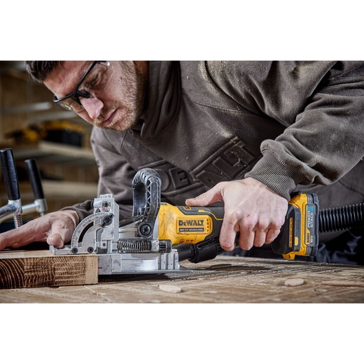 A PERSON USING A DCW682 18V XR BISCUIT JOINTER WITH A 5AH BATTERY ON OAK TIMBER IN A WORKSHOP