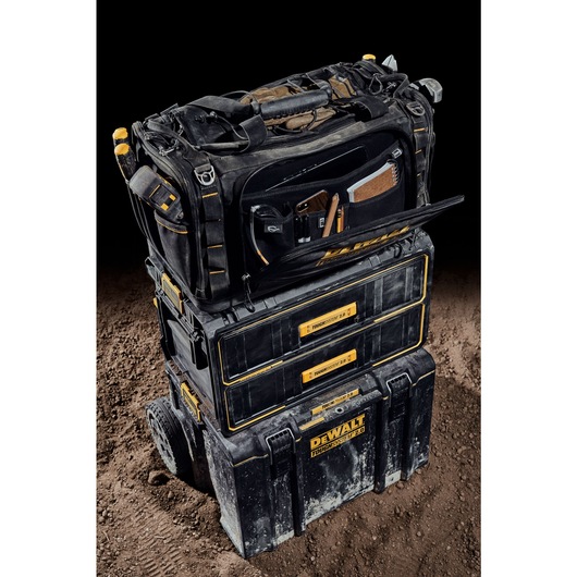 Front view of the DEWALT TOUGHSYSTEM 2.0 22-inch jobsite soft storage toolbag with front pocket open holding various tools on top of TOUGHSYSTEM 2.0 two-drawer organizer.